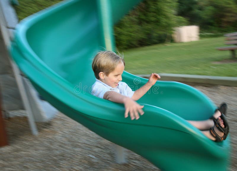 Young boy sliding down a green park slide. Young boy sliding down a green park slide