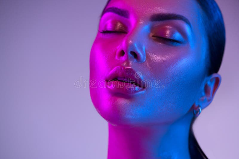 Glossy, wet skin makeup. Fashion model woman face in bright neon colourful lights, beautiful woman, UV, ultraviolet trendy make-up