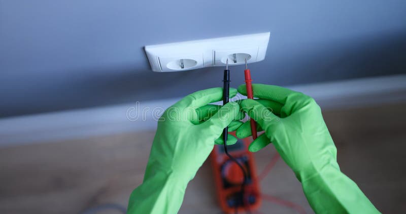Gloved hands are holding a digital multimeter near the socket stock images