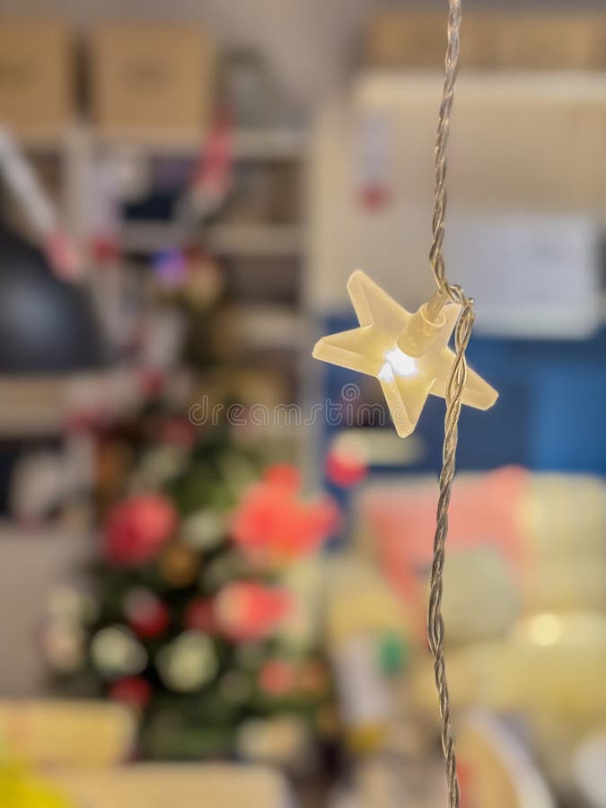 Glowing single yellow translucent star shaped led light on a twisted wire string in the foreground, festive christmas stock photo