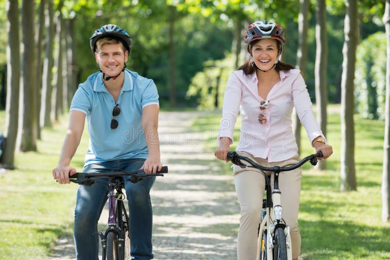 Glückliche junge Paare, die in Park radfahren lizenzfreies stockbild Glückliche junge Paare, die in Park radfahren lizenzfreies stockbild