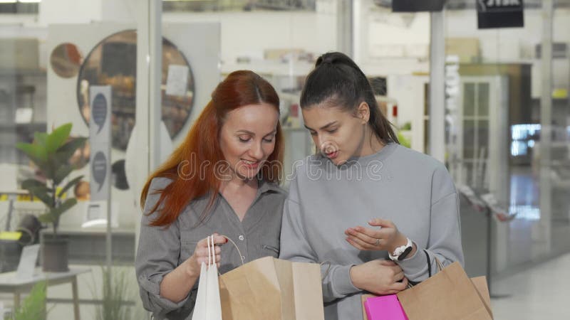 Glädjande unga kvinnor som kramar och tittar i sina shoppingväskor vid köpcentret