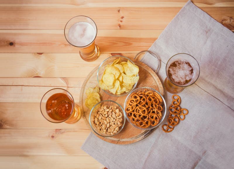 Gläser helles Bier mit Kartoffelchips, gesalzenen Brezeln und Erdnüssen auf Holztisch lizenzfreie stockfotos Gläser helles Bier mit Kartoffelchips, gesalzenen Brezeln und Erdnüssen auf Holztisch lizenzfreie stockfotos