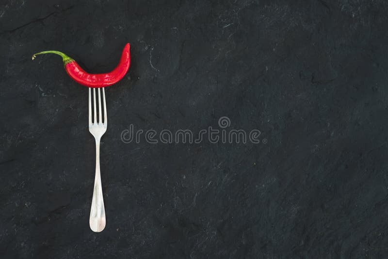 Red hot chili pepper on vintage silver fork over black slate stone background, top view, copy space copy space space copy space space. Red hot chili pepper on vintage silver fork over black slate stone background, top view, copy space copy space space copy space space