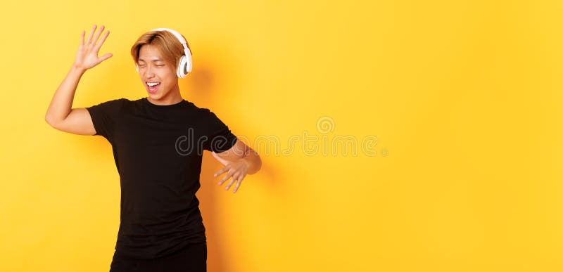 Glücklich attraktiver asiatischer Typ mit blonden Haaren, der mitsingt und tanzt, als er Musik in drahtlosen Kopfhörern hört stockfoto