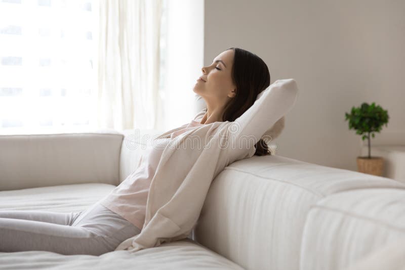 Happy millennial woman relaxing on sofa, breathing cool air from conditioner, enjoying comfortable climate in ventilated living room, meditating with closed eyes. Comfort at home, conditioning concept. Happy millennial woman relaxing on sofa, breathing cool air from conditioner, enjoying comfortable climate in ventilated living room, meditating with closed eyes. Comfort at home, conditioning concept