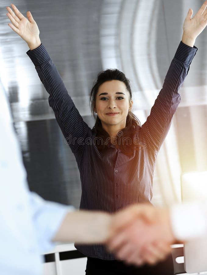 Glücklich und aufgeregt Geschäftsfrau erhebt Hände wegen Erfolg Vereinbarung bei der Sitzung. zwei Männer die Hände schütteln in s lizenzfreies stockfoto