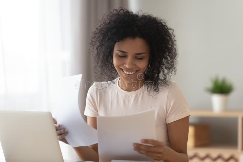 Glückliche afrikanische Frau sitzen bei Tisch, Papierprüfungsrechnungen lesend lizenzfreie stockfotos Glückliche afrikanische Frau sitzen bei Tisch, Papierprüfungsrechnungen lesend lizenzfreie stockfotos
