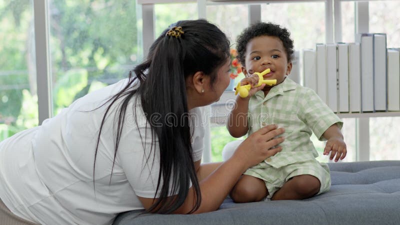 Glückliche asiatische Mutter spielt mit kleinen Kleinkindern Kind auf Wohnzimmersofa. Eltern und kleine Kinder entspannen zu Hause