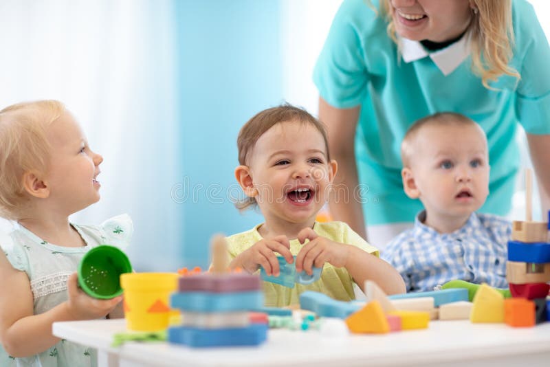 Glückliche Babys in der Tagespflege. Gruppe von Kindern, die Spielzeug mit Kindergärtnerin spielen. Kinderstunde in Kinderkrippe