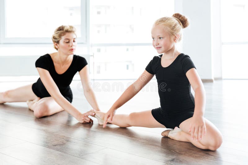 Glückliche Ballerina des kleinen Mädchens, die Beine mit Lehrer sitzt und ausdehnt