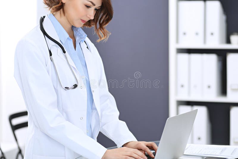 Glückliche Doktorfrau bei der Arbeit Porträt des weiblichen Arztes, der Laptop-Computer bei der Stellung des nahen Aufnahmeschrei