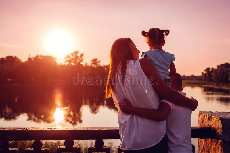 Glückliche Familie, welche die Zeit draußen umarmt und genießt die Ansicht von Fluss bei Sonnenuntergang verbringt Mutter mit zwe stockbilder Glückliche Familie, welche die Zeit draußen umarmt und genießt die Ansicht von Fluss bei Sonnenuntergang verbringt Mutter mit zwe stockbilder