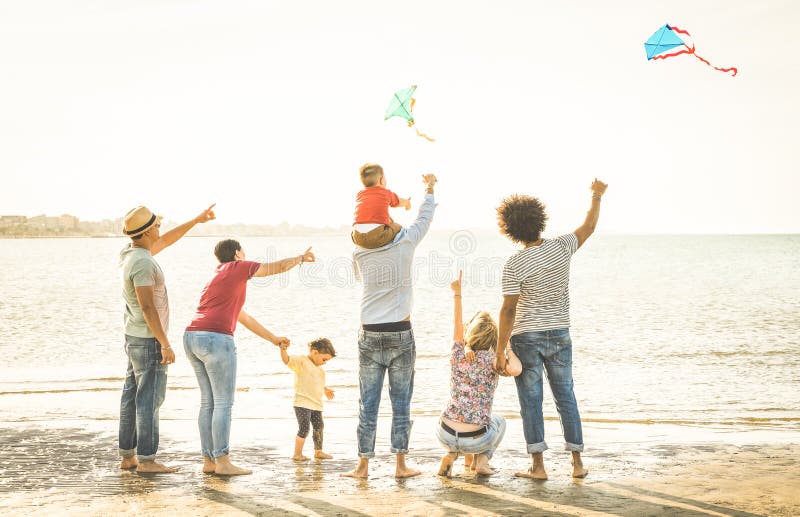 Glückliche Familiengruppe mit den Eltern und Kindern, die mit Drachen am Strand spielen stockbilder