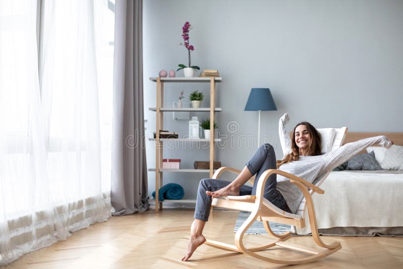 Glückliche Frau, die auf modernem Stuhl im Wohnzimmer bequem zu Hause sitzen stillsteht Glückliche Frau, die auf modernem Stuhl im Wohnzimmer bequem zu Hause sitzen stillsteht