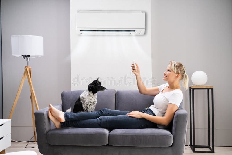 Glückliche Frau, die auf Sofa mithilfe der Klimaanlage sitzt lizenzfreies stockfoto