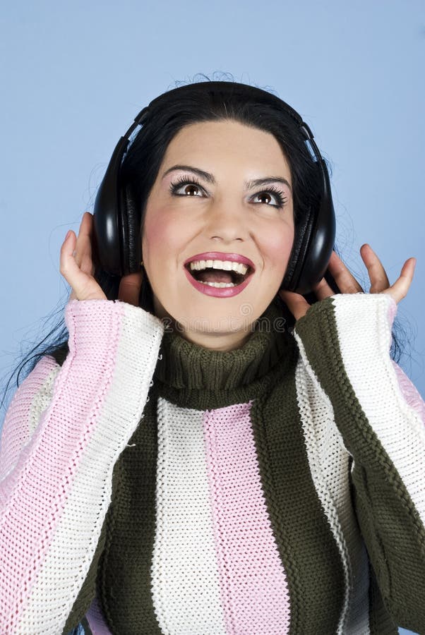 Happy brunette woman in pullover enjoying music in headphones,smiling ,singing , looking up and holding hands on head over blue background,check also my photos in this collection. Happy brunette woman in pullover enjoying music in headphones,smiling ,singing , looking up and holding hands on head over blue background,check also my photos in this collection