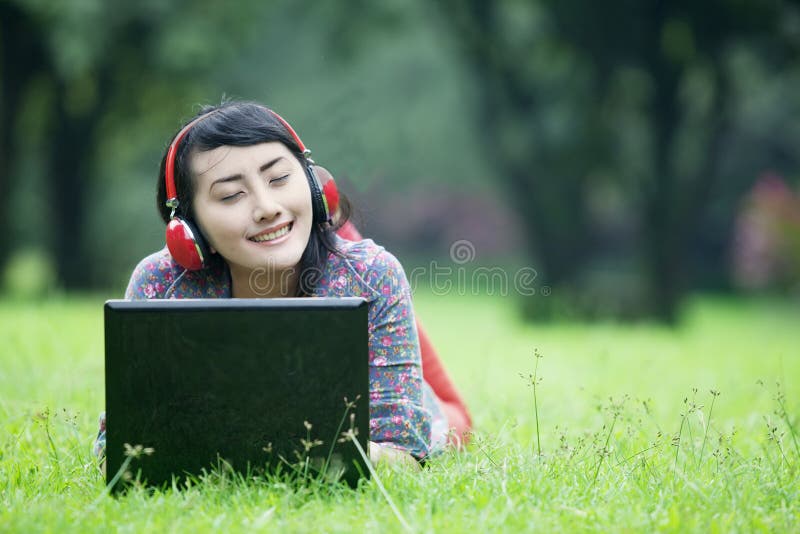 A happy woman relaxing at the park while enjoying music using her headphone. A happy woman relaxing at the park while enjoying music using her headphone