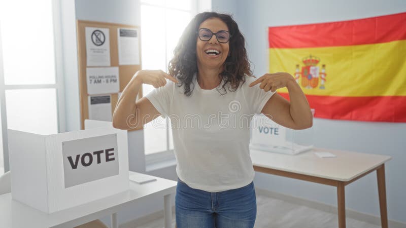 Glückliche Frau, die sich in einem spanischen Wahlzimmer mit einer Spain-Fahne im Hintergrund zeigt und so eine einnehmende und fr stockbild