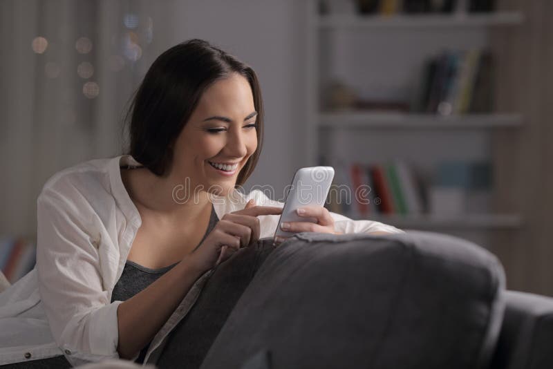 Glückliche Frau, die Telefon in der Nacht auf einer Couch verwendet stockbilder