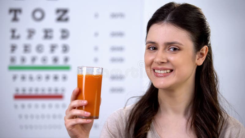 Glückliche Frau trinkt gesunden frischen Karottensaft, Augendiagramm auf dem Hintergrund, Sehvermögen lizenzfreies stockbild Glückliche Frau trinkt gesunden frischen Karottensaft, Augendiagramm auf dem Hintergrund, Sehvermögen lizenzfreies stockbild
