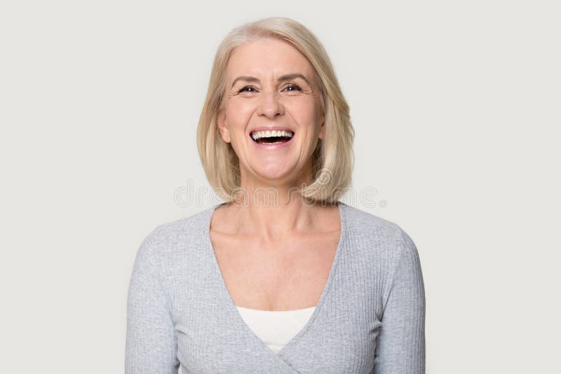 Glückliche gealterte weibliche lachende Aufstellung des Headshot auf grauem Studiohintergrund