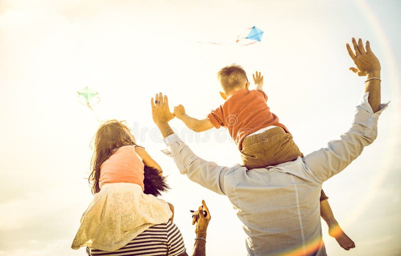 Glückliche gemischtrassige Familiengruppe mit den Eltern und Kindern, die mit Drachen an den Strandferien - Sommerfreudenkonzept lizenzfreies stockbild