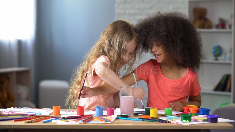 Glückliche gemischtrassige Freunde, die mit Aquarellen im Kindergarten, Hobby malen lizenzfreie stockfotografie Glückliche gemischtrassige Freunde, die mit Aquarellen im Kindergarten, Hobby malen lizenzfreie stockfotografie