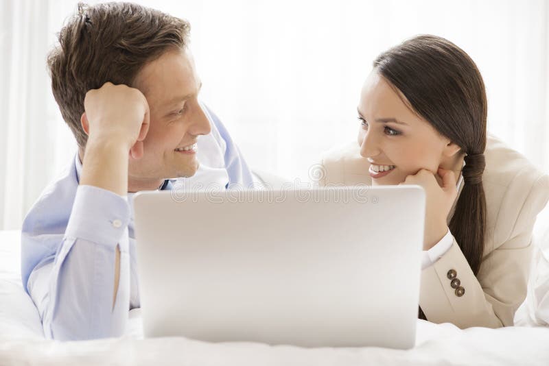 Glückliche Geschäftspaare mit dem Laptop, der einander im Hotel betrachtet lizenzfreies stockfoto Glückliche Geschäftspaare mit dem Laptop, der einander im Hotel betrachtet lizenzfreies stockfoto