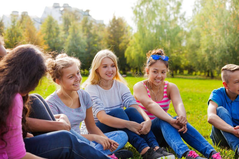 Glückliche internationale Freunde sitzen zusammen auf Wiese lizenzfreies stockfoto