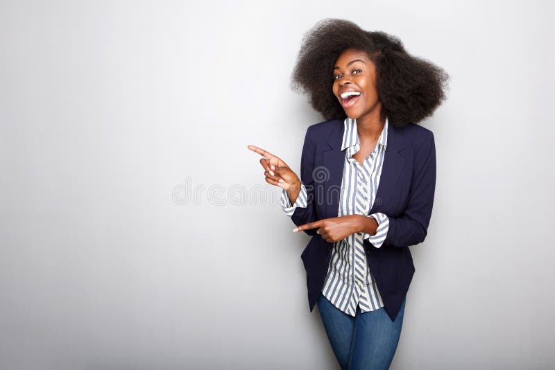 Glückliche junge Afroamerikanerfrau, die Finger gegen grauen Hintergrund zeigt