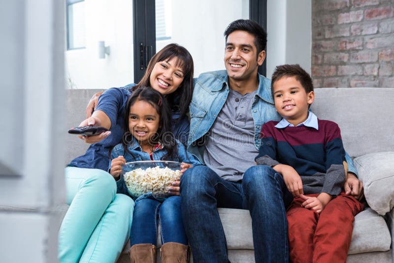 Glückliche junge Familie, die Popcorn beim Fernsehen isst lizenzfreies stockbild Glückliche junge Familie, die Popcorn beim Fernsehen isst lizenzfreies stockbild