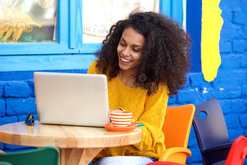 Glückliche junge Frau, die Café am im Freien unter Verwendung des Laptops sitzt stockfoto