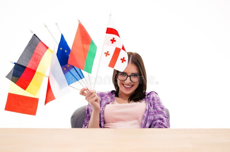 Glückliche junge Frau, die am Tisch mit internationalen Flaggen sitzt lizenzfreie stockfotografie Glückliche junge Frau, die am Tisch mit internationalen Flaggen sitzt lizenzfreie stockfotografie