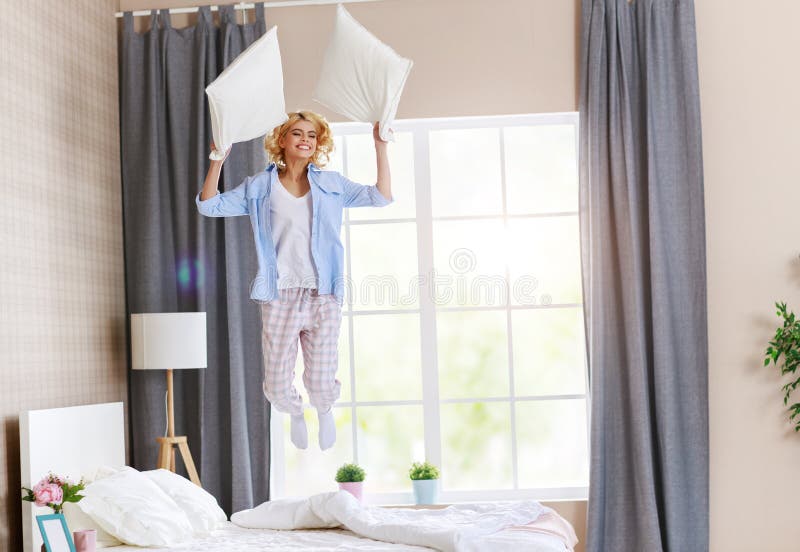 Glückliche junge Frau, die zu Hause auf das Bett am Morgen lacht und springt stockbilder