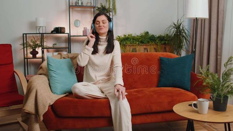 Glückliche junge Frau in drahtlosen Kopfhörern entspannt auf Sofa zu Hause Musik hören