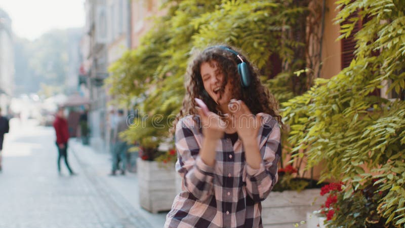 Glückliche junge Frau in drahtlosen Kopfhörern hört Lieblingsmusik in städtischen Straßen