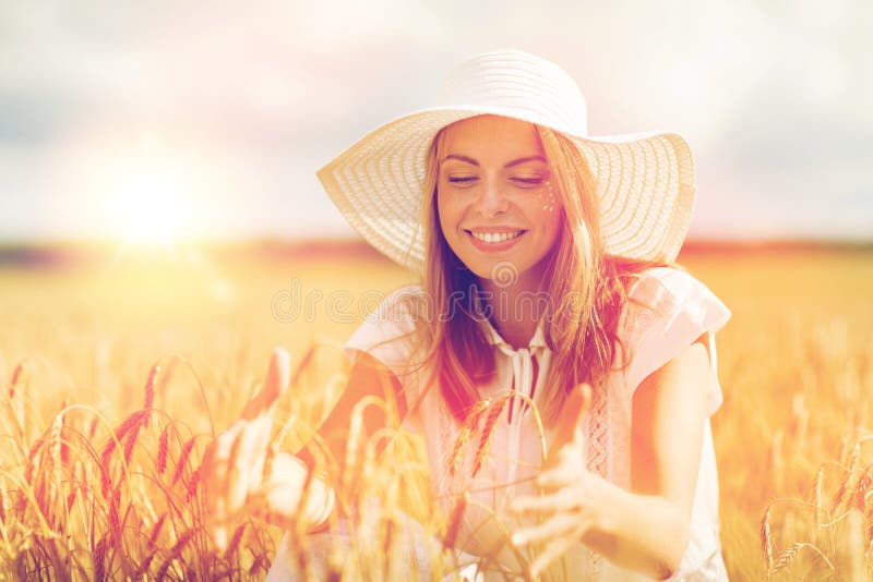 Nature, summer holidays, vacation and people concept - happy young woman in white dress and sun hat enjoying sun on cereal field. Nature, summer holidays, vacation and people concept - happy young woman in white dress and sun hat enjoying sun on cereal field