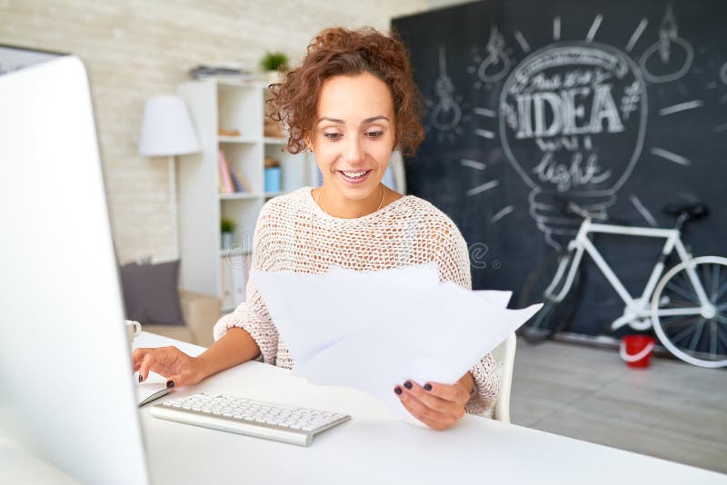 Glückliche junge Frauen-Lesegeschäftsunterlagen am Schreibtisch lizenzfreies stockfoto Glückliche junge Frauen-Lesegeschäftsunterlagen am Schreibtisch lizenzfreies stockfoto