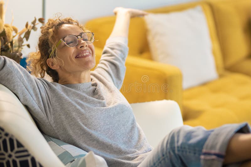 Glückliche junge kaukasische Frau, die auf einem Stuhl zu Hause im Wohnzimmer sitzt, öffnete ihre Arme und lächelt viel. Erfolg un stockfoto