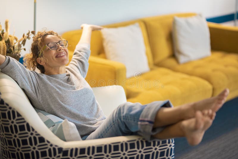 Glückliche junge kaukasische Frau, die zu Hause im Wohnzimmer auf einem Stuhl sitzt, öffnete ihre Arme und lächelt viel. Erfolg un stockfoto
