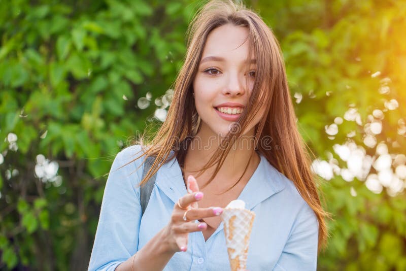 Glückliche junge lächelnde Brunettefrau, die Eiscreme auf grünen Bäumen isst lizenzfreie stockfotografie Glückliche junge lächelnde Brunettefrau, die Eiscreme auf grünen Bäumen isst lizenzfreie stockfotografie