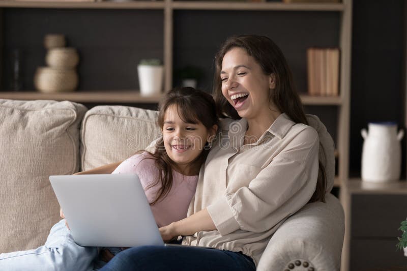 Glückliche junge Mutter kleine Tochter lachen über Film auf Notebook stockfotografie