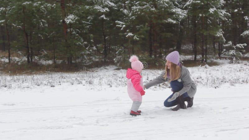 Glückliche junge Mutterspiele mit ihrem wenigen Schneebaby im Winterwald