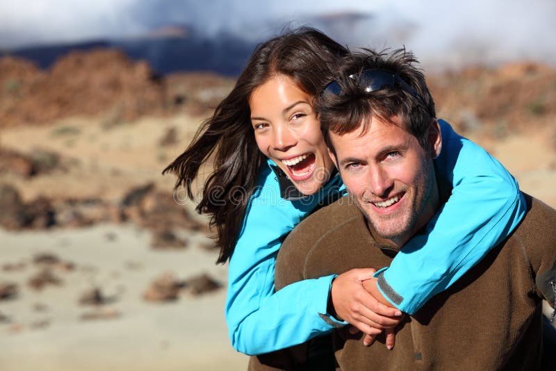 Happy young couple smiling outdoors piggybacking during hiking travel. Young Asian / Caucasian hikers couple cheerful on volcano Teide, Tenerife, Canary Islands. Happy young couple smiling outdoors piggybacking during hiking travel. Young Asian / Caucasian hikers couple cheerful on volcano Teide, Tenerife, Canary Islands.