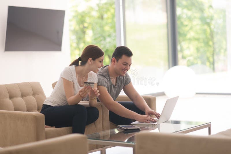 Happy young couple buying online using laptop a computer and a credit card in their luxury home villa. Happy young couple buying online using laptop a computer and a credit card in their luxury home villa