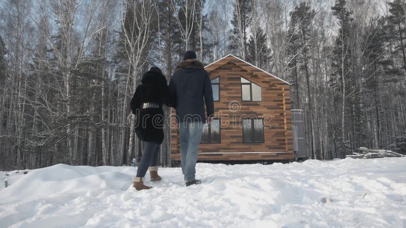 Glückliche junge Paare nahe hölzernem Häuschen ablage Verbinden Sie Stände nahe dem Haus im Wald im Winter