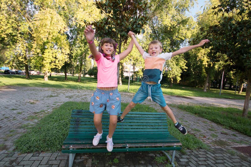 Glückliche Kinder amüsieren sich beim Springen von der Bank auf dem Park lizenzfreies stockfoto