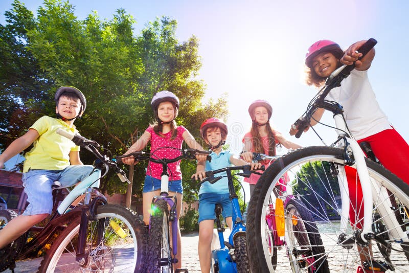 Group of multiethnic children in safety helmets, standing with their bicycles in summer park. Group of multiethnic children in safety helmets, standing with their bicycles in summer park