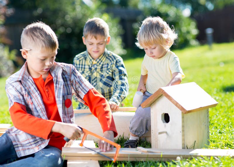 Glückliche Kinderbrüder, die hölzernes Vogelhaus durch Hände machen lizenzfreies stockfoto Glückliche Kinderbrüder, die hölzernes Vogelhaus durch Hände machen lizenzfreies stockfoto
